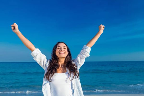 A woman smiling with her hands raised above her head on the beach