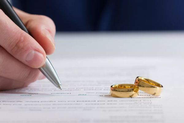 A person signing divorce papers with two gold rings