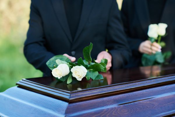 People placing white roses on a coffin