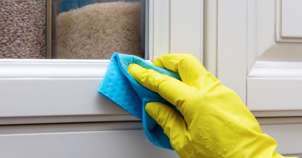 Cleaning and wiping the doors of the facade of the kitchen cabinet. Hand in a yellow glove with a blue rag